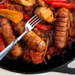 cast iron pan with sausages and bell peppers in tomato sauce
