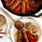Two sausages with sauce and bell peppers served on a plate.