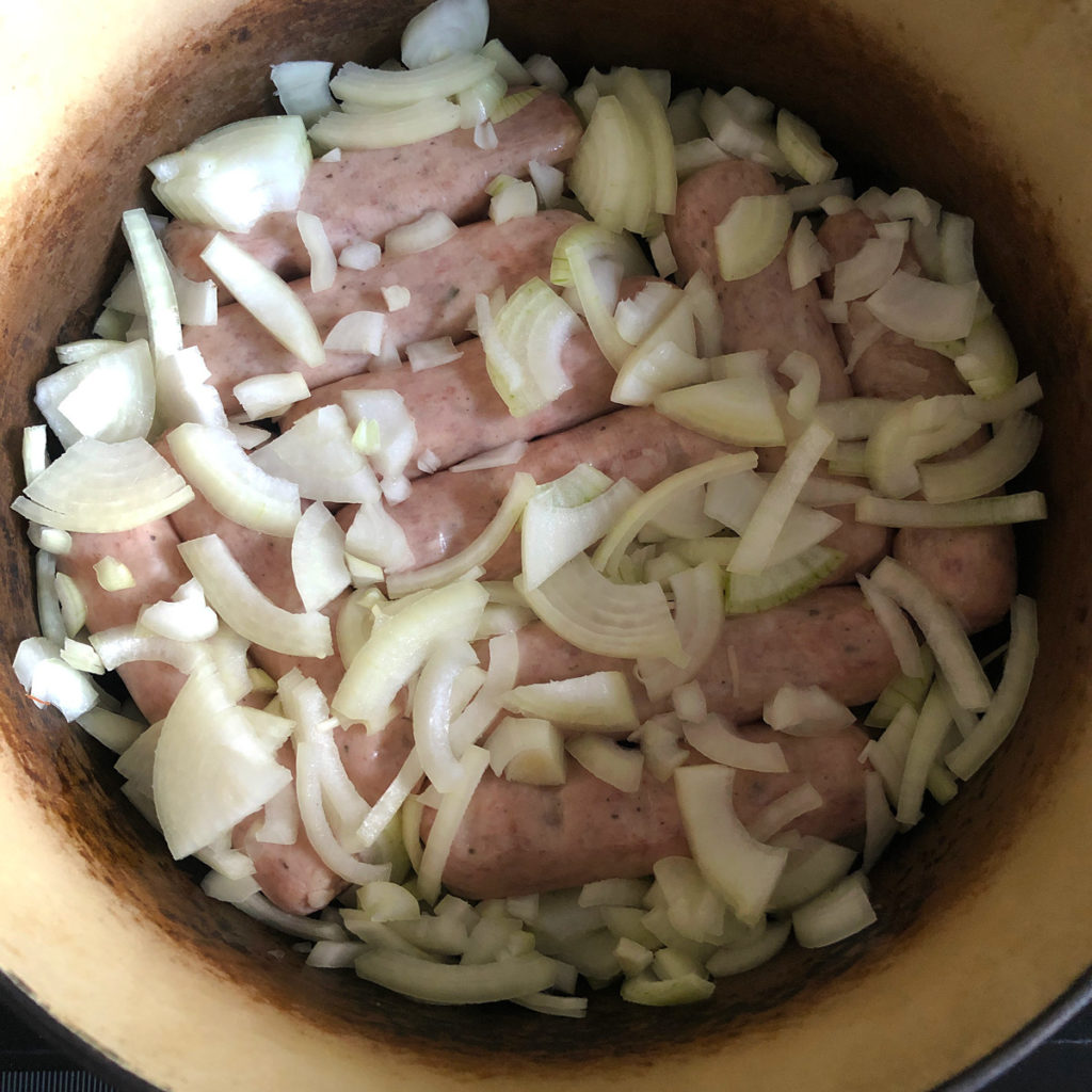 Raw pork sausages in a cast iron pot, coverd with sliced onion.