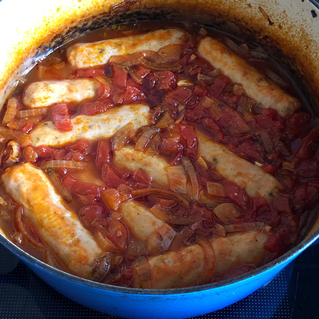 Sausages and tomato-based stock in a pot after 45 minutes in the oven.