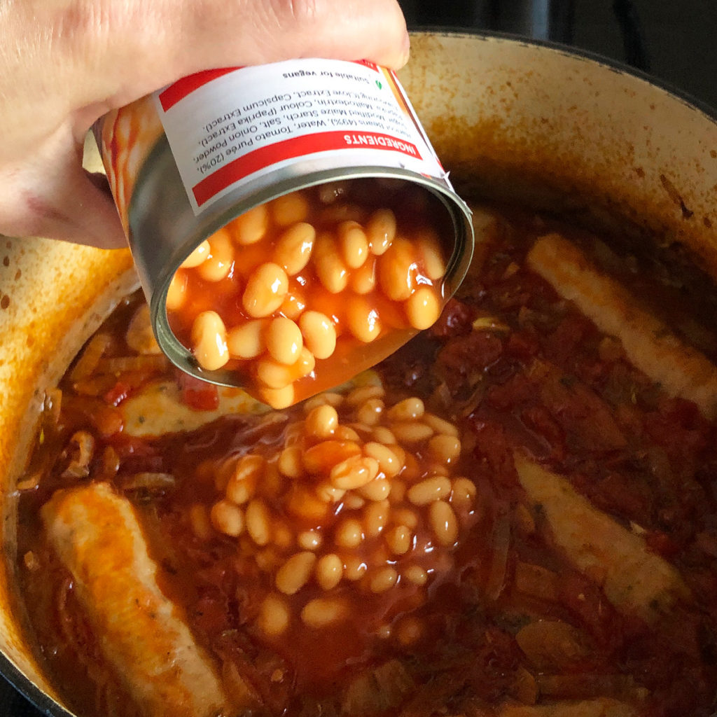 Adding baked beans into a sausage hotpot.
